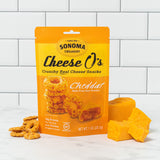 a bag of our cheddar cheese O's displayed in front of a white tile background with the ingredients arranged at the base