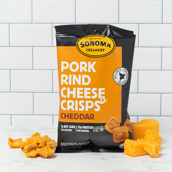a bag of our Cheddar Pork Rind Cheese Crisps displayed in front of a white tile background with the ingredients arranged at the base